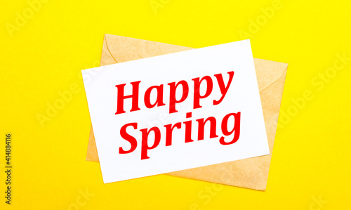 On a yellow background, an envelope and a card with the text HAPPY SPRING. View from above