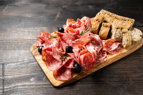 Sliced salumi salami on a wooden board with olives and multigrain baguette. italian food, appetizer for aperitif or salami sandwich. Top view