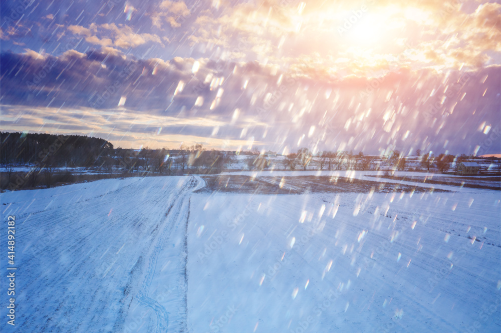 Rural landscape in winter. The field is covered with snow at sunset with a dramatic cloudy sky.
