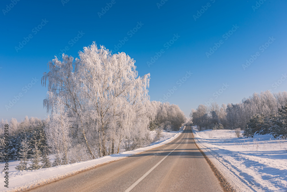 Obraz premium Winter landscape with the road the forest and the blue sky