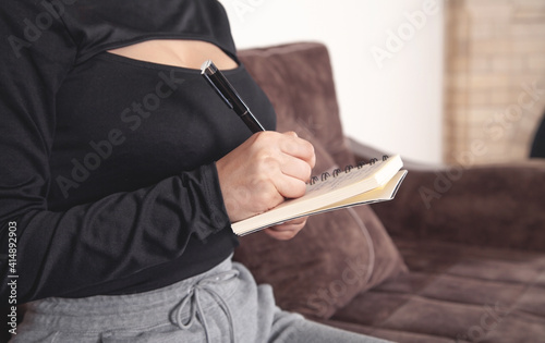 Young woman sitting in sofa writes in notepad.