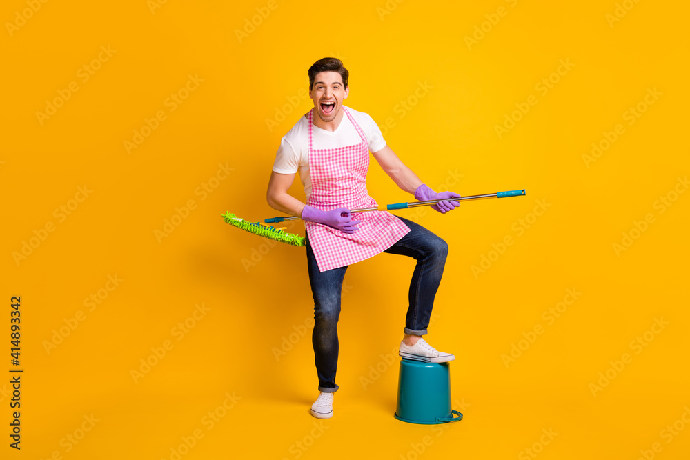 Full size portrait of positive man put leg on bucket hands playing guitar mop isolated on yellow color background Full size portrait of positive man put leg on bucket hands playing guitar mop isolated on yellow color background