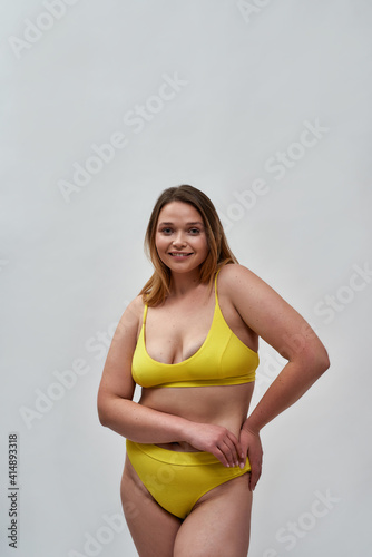 Attractive curvy young female model wearing yellow underwear looking at camera while posing isolated over light background