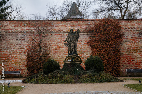 St. John of Nepomuk baroque statue, Czech patron Jan Nepomucky, Benedictine monastery Brevnov, brick walls, Garden and park, abbey under snow in winter day, Prague, Czech Republic photo