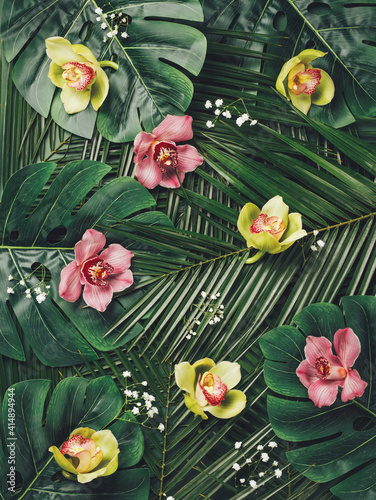 Tropical layout made with exotic palm leaves and vibrant fresh orchid flowers. Creative spring or summer background. Floral or natural visual trend. Flat lay, top view.