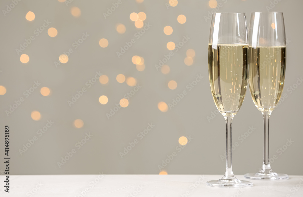 Glasses of champagne on grey table against blurred lights. Space for text Glasses of champagne on grey table against blurred lights. Space for text