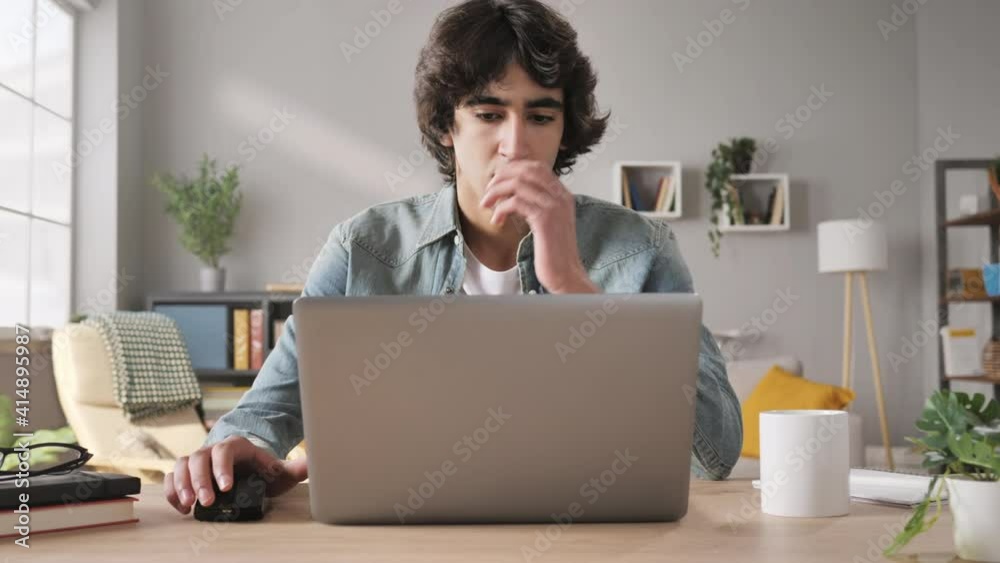frustrated upset man sits at his desk opens laptop zoom out motion,young male student feel stressed using notebook computer looking annoyed at the screen sitting at home office table failure concept