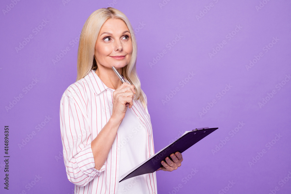 Photo of sweet dreamy lady pensioner wear striped shirt holding clipboard looking empty space isolated violet color background Photo of sweet dreamy lady pensioner wear striped shirt holding clipboard looking empty space isolated violet color background