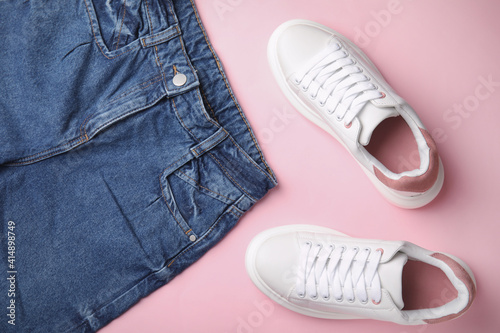 Stylish white sneakers and jeans on pink background, flat lay