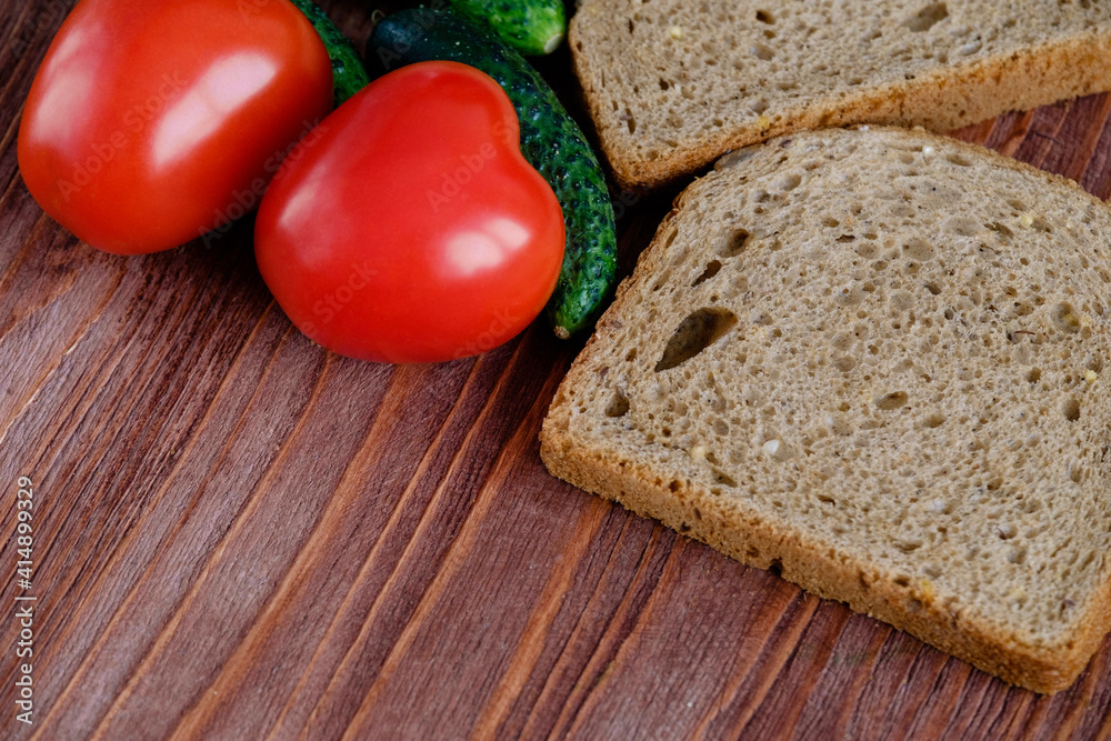 Two heart-shaped tomatoes lie on a wooden table along with bread and gherkins. Flat lay. Close up. Copy space Two heart-shaped tomatoes lie on a wooden table along with bread and gherkins. Flat lay. Close up. Copy space