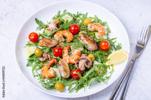 Salad with seafood, arugula, tomatoes, cucumbers and olives on a white plate. Close-up.