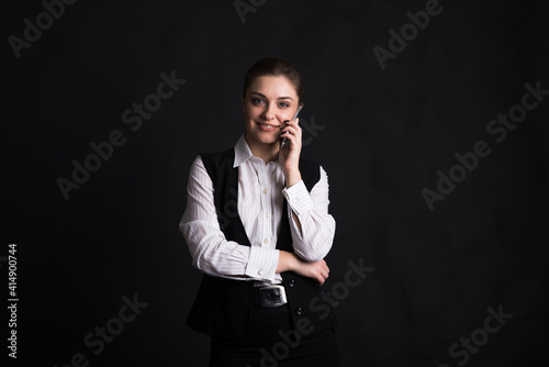Portrait of a female business lady who is talking on the phone in the studio on a black background