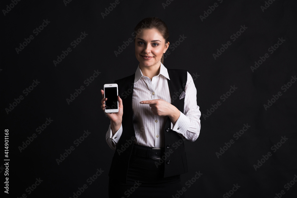 Portrait of a female business lady who points with a finger at the screen of her smartphone in the studio on a black background