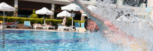 Man swim with breast stroke in blue pool of clear water. Splashes of water fly to sides.