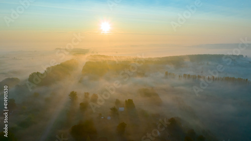 Aerial view of early morning mist over small rustic road among forest trees