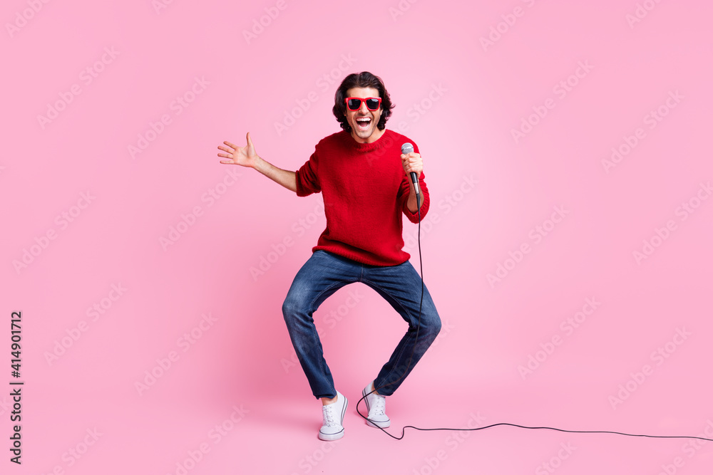 Photo portrait of dancing singing man holding microphone in hand wearing sunglasses isolated on pastel pink colored background