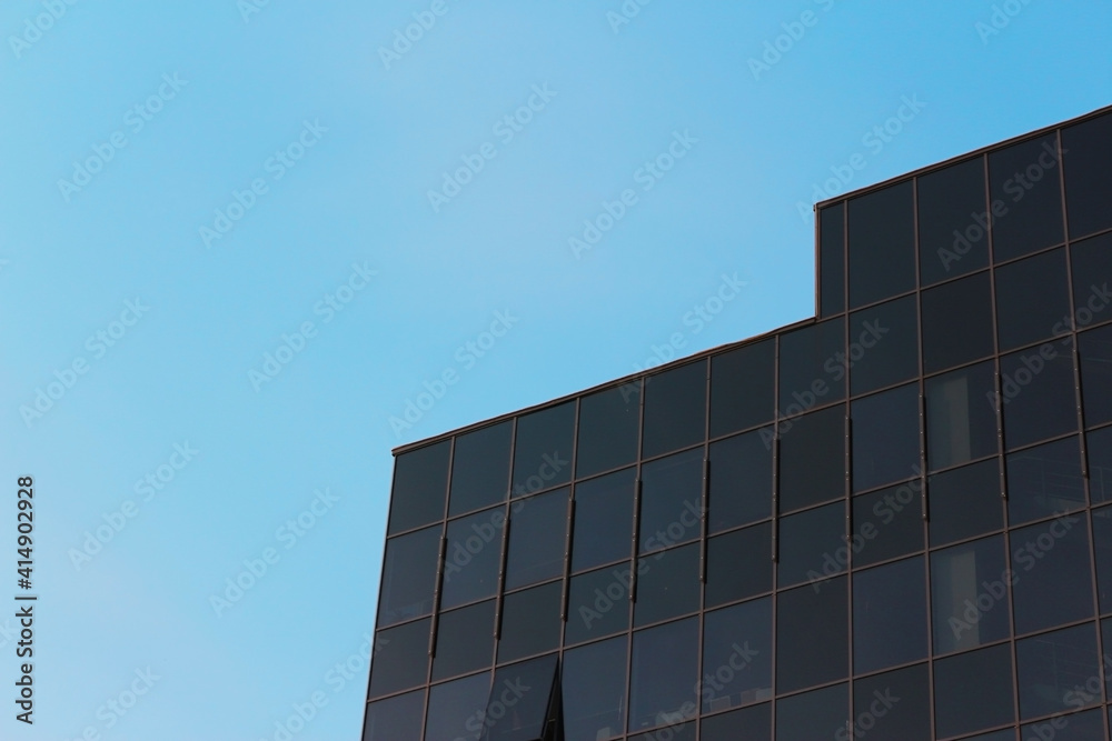 Part of a modern dark office building against the blue sky