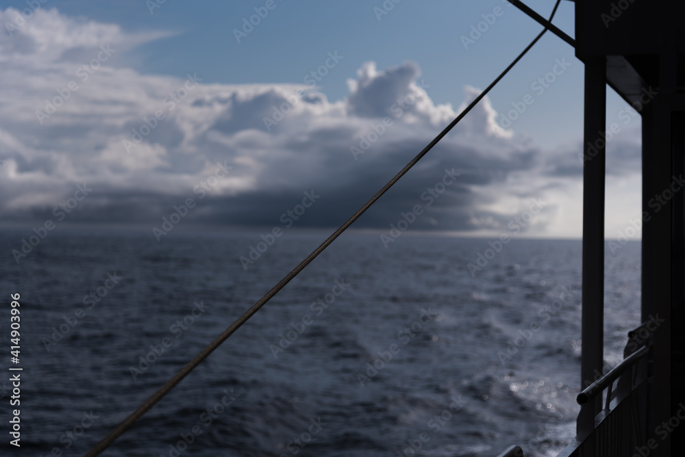 A view of the open, deep blue sea from the railing of a passenger ship - in the background you can see how a storm or thunderstorm is formed on the sea - dark, black clouds  - steel rope