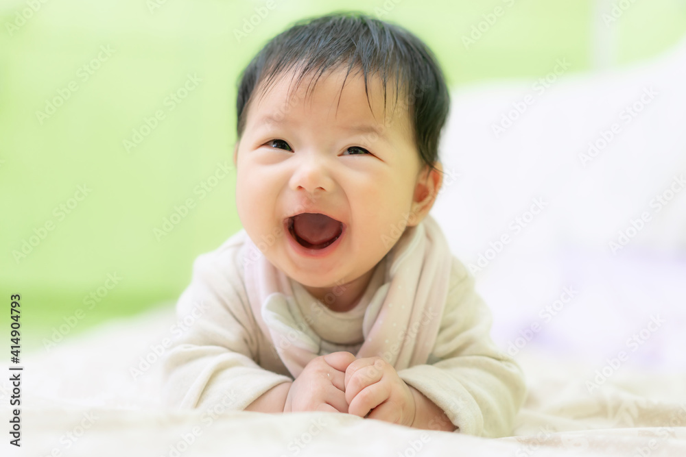 Asian Happy newborn baby smiling while lying down on the bed. 3 Months cute baby laughing on the bed use as baby development and education concept.