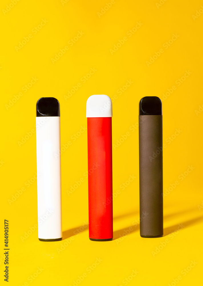Colorful disposable electronic cigarettes with shadows on a yellow background. The concept of modern smoking, vaping and nicotine. Colorful disposable electronic cigarettes with shadows on a yellow background. The concept of modern smoking, vaping and nicotine.