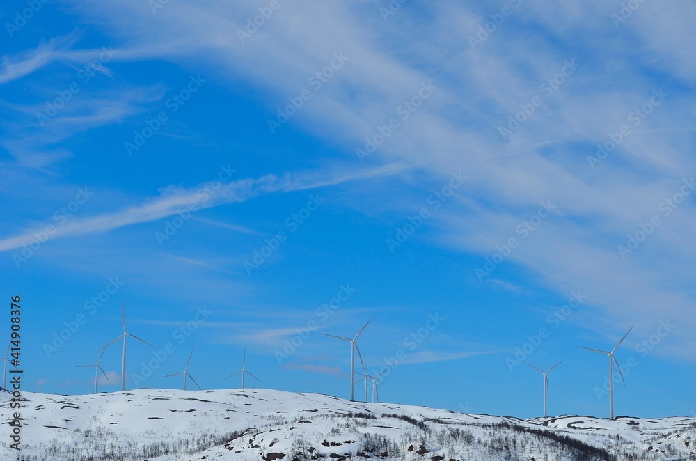 windmill farm on snowy mountain in northern Norway in bright sunshine and blue sky backdrop