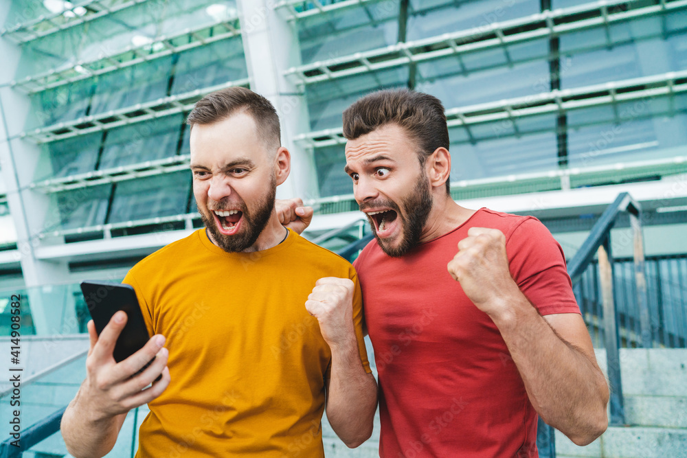 Men being happy winning a bet in online sport gambling application with football stadium on the background Men being happy winning a bet in online sport gambling application with football stadium on the background