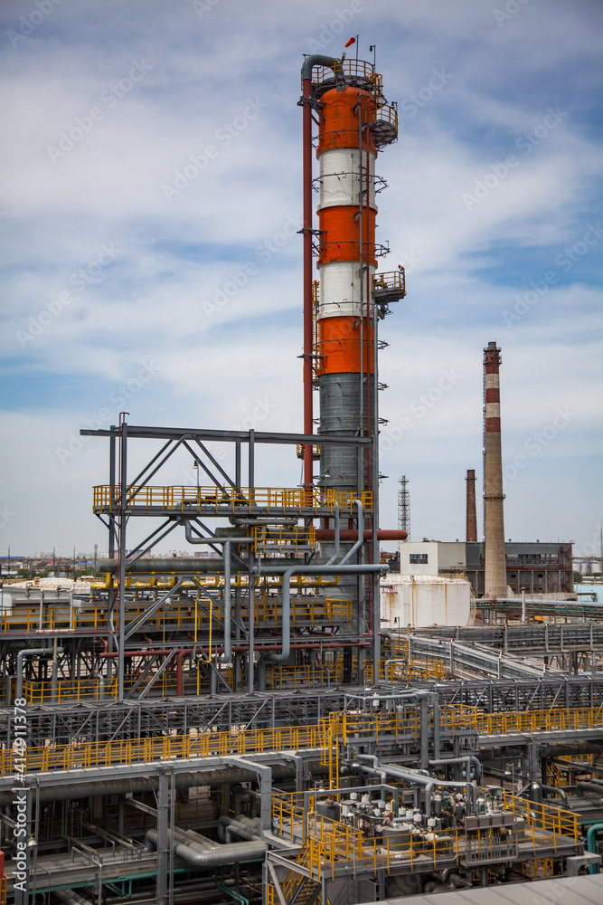 Oil refinery plant. Red and white striped distillation tower (column) and smoke stack. On blue sky background.
