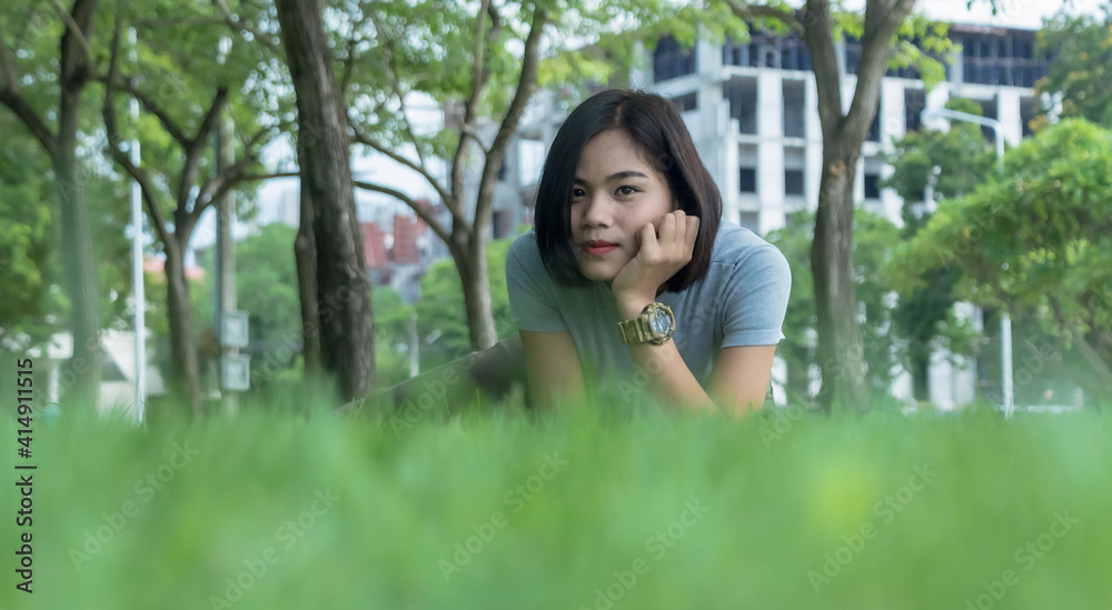 Portrait of young Asian woman enjoying and relaxing outdoors. Cheerful teenage female sitting on the green grass in the park on a sunny summer day. Portrait of young Asian woman enjoying and relaxing outdoors. Cheerful teenage female sitting on the green grass in the park on a sunny summer day.