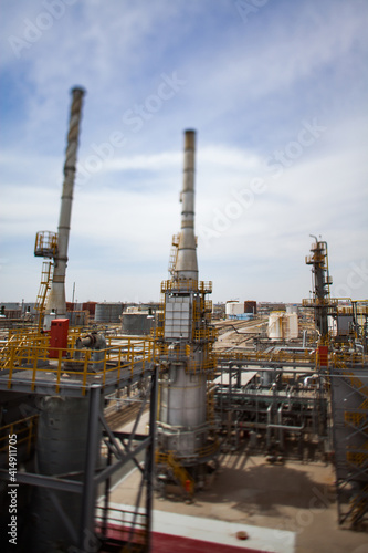 Oil refinery complex in desert. columns and chimneys. Tilt-shift blurred effect. Blue sky with clouds. Vertical photo