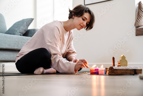Fotografie, Obraz Peaceful girl lighting candles while sitting at home shrine
