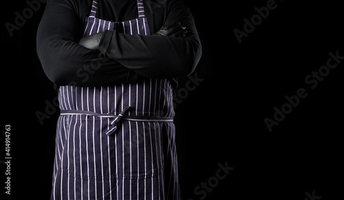  man chef in a striped blue apron and black clothes stands against a black background
