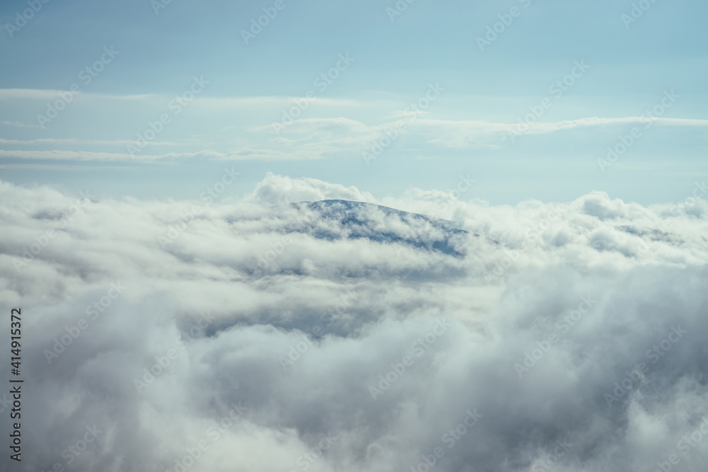 Wonderful minimalist landscape with mountain top above dense low clouds. Mountain vertex floats in thick clouds. Scenic minimalism with mountain peak above cloudy sky. Beautiful summit in cloudiness.