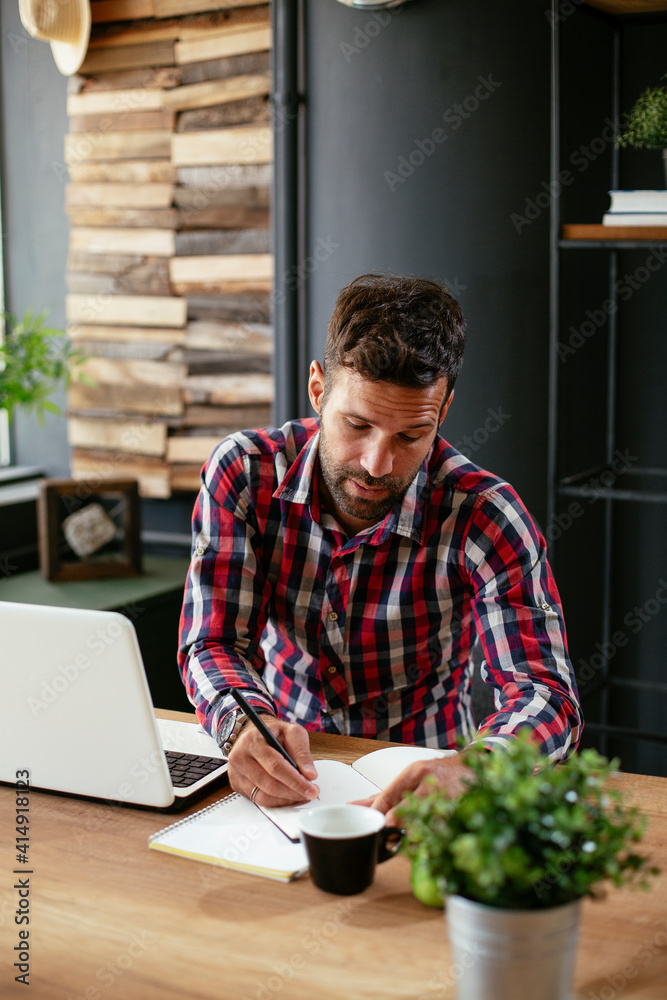Businessman taking a notes while working on laptop. Young businessman writing in a notebook Businessman taking a notes while working on laptop. Young businessman writing in a notebook