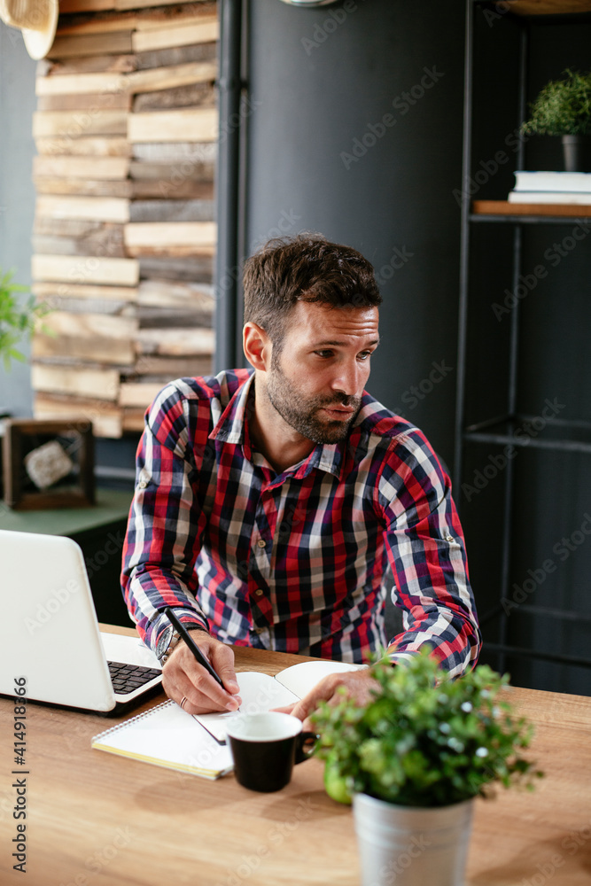 Businessman taking a notes while working on laptop. Young businessman writing in a notebook