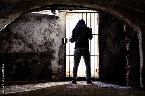 Fototapeta Prisoner man locked up standing in old underground cellar , silhouette from behi