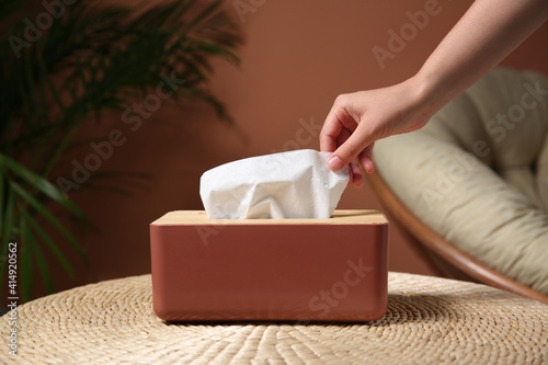 Woman taking paper tissue out of box on table indoors, closeup photo
