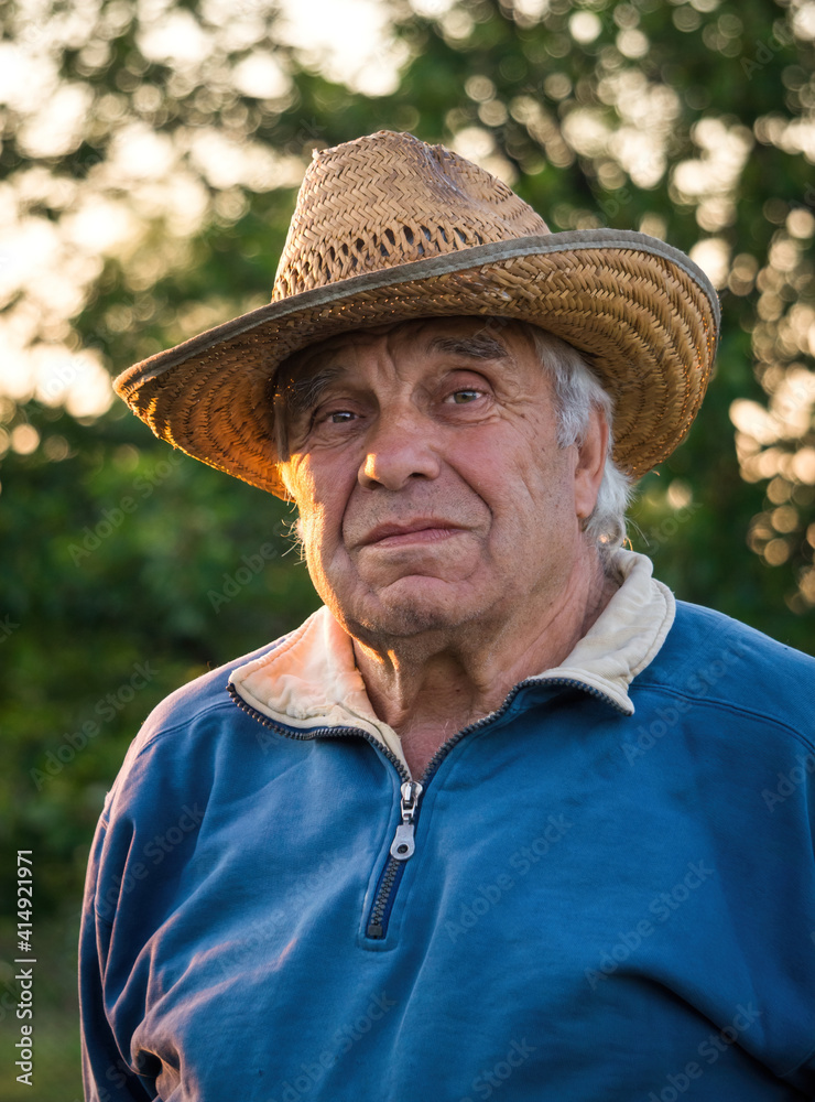 Elderly man in a straw hat on the background of the evening summer garden