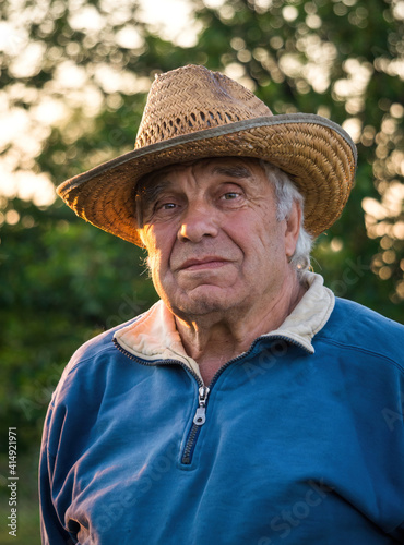 Elderly man in a straw hat on the background of the evening summer garden