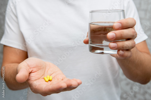 yellow tablets and a glass of water in men's hands
