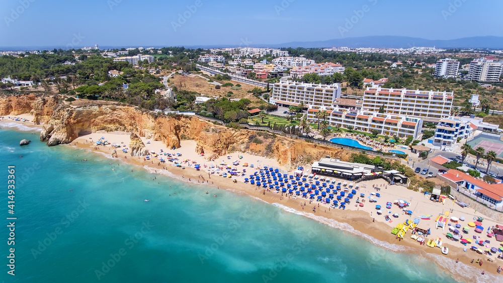 Aerial drone shot of a busy beach, amazing cliffs, vegetation and also buidlings in the background. Praia do Vau, Portimao, Portugal.