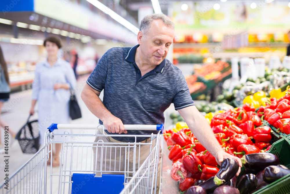 Mature man examines eggplant  in the vegetables section of the supermarket