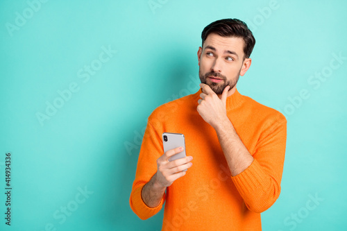 Photo of young handsome man use cellphone hand touch chin think dream look empty space isolated over turquoise color background photo