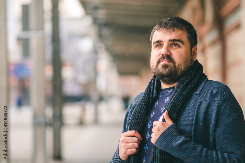 Bearded guy in blue sweater standing on the street with his hands on his scarf, looking up. Bearded guy in blue sweater standing on the street with his hands on his scarf, looking up.