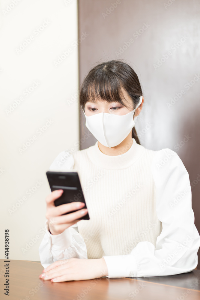 Woman in a mask sitting on a chair and holding a smartphone