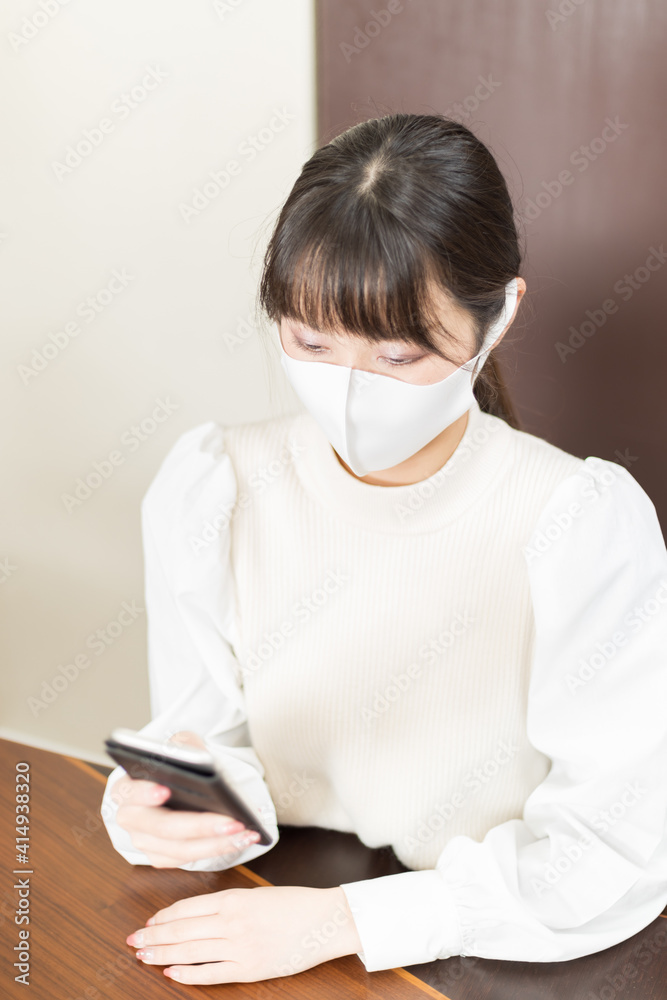 Woman in a mask sitting on a chair and holding a smartphone