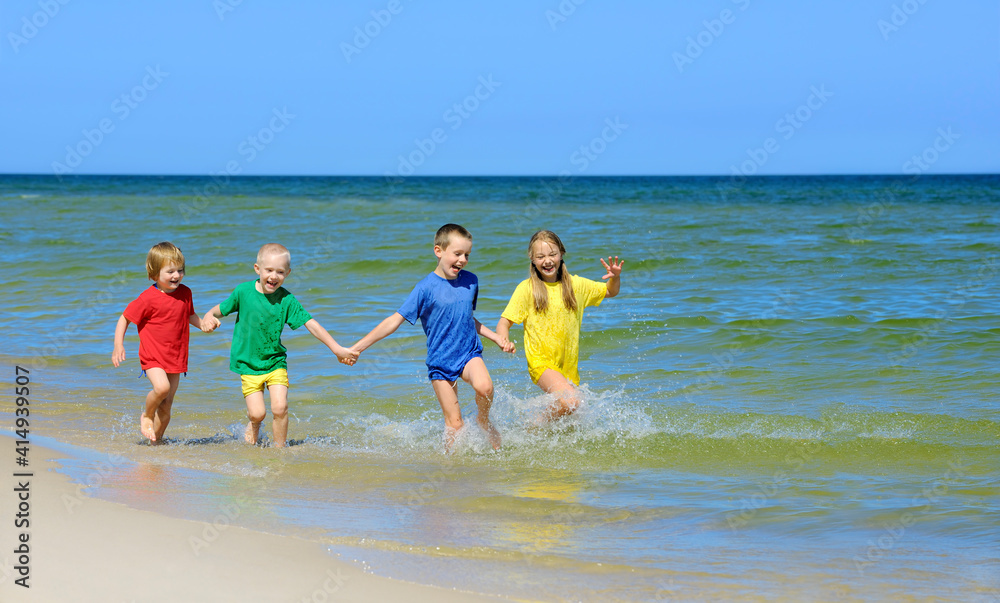 Two girls and two boys in colorful t-shirts running on sandy beach