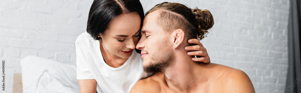 Brunette woman kissing shirtless boyfriend in bedroom, banner Brunette woman kissing shirtless boyfriend in bedroom, banner
