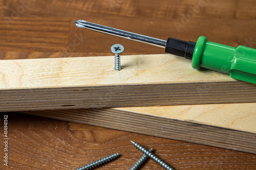 Woodwork. Wooden slats and working tools. Metal screw and screwdriver. Self-tapping screw screwed into a wooden lath.
