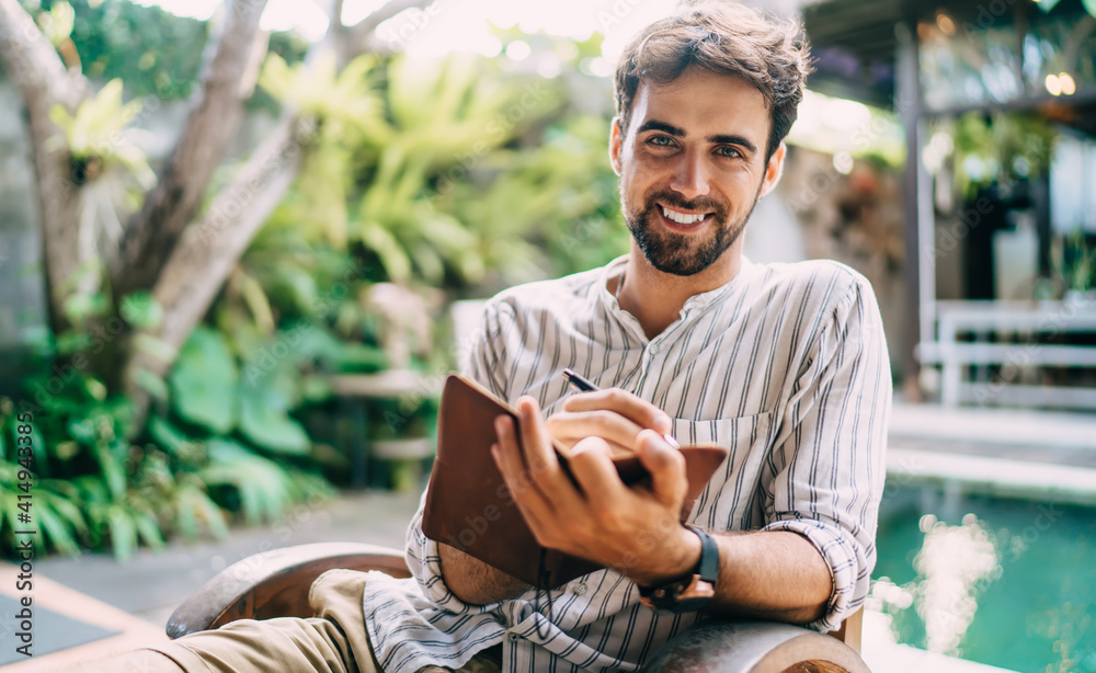 Fototapeta premium Happy man writing in notebook near swimming pool