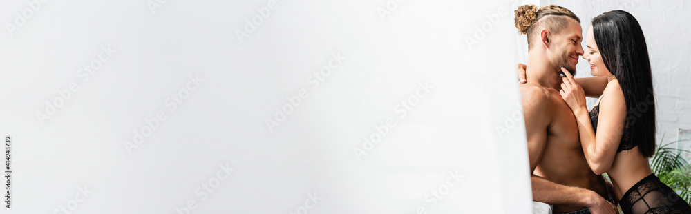 Side view of smiling couple kissing near curtain on blurred foreground at home, banner Side view of smiling couple kissing near curtain on blurred foreground at home, banner
